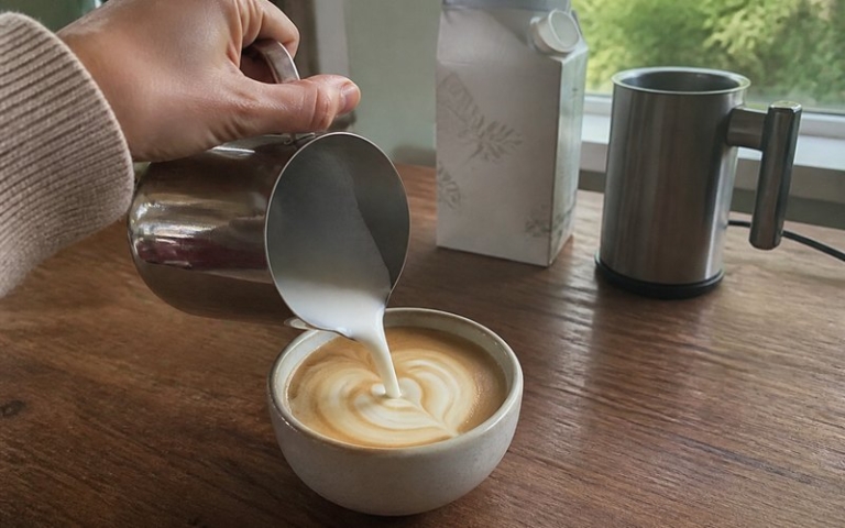 Aufgeschäumte Pflanzenmilch wird in den Kaffee gegossen